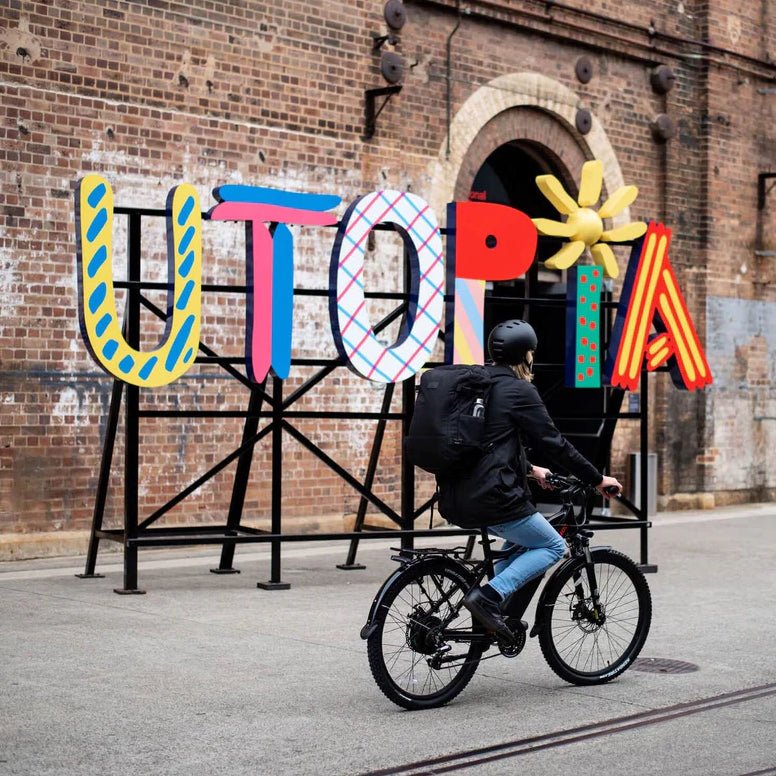 A person rides a bicycle past a large, colorful, outdoor typographic sculpture
