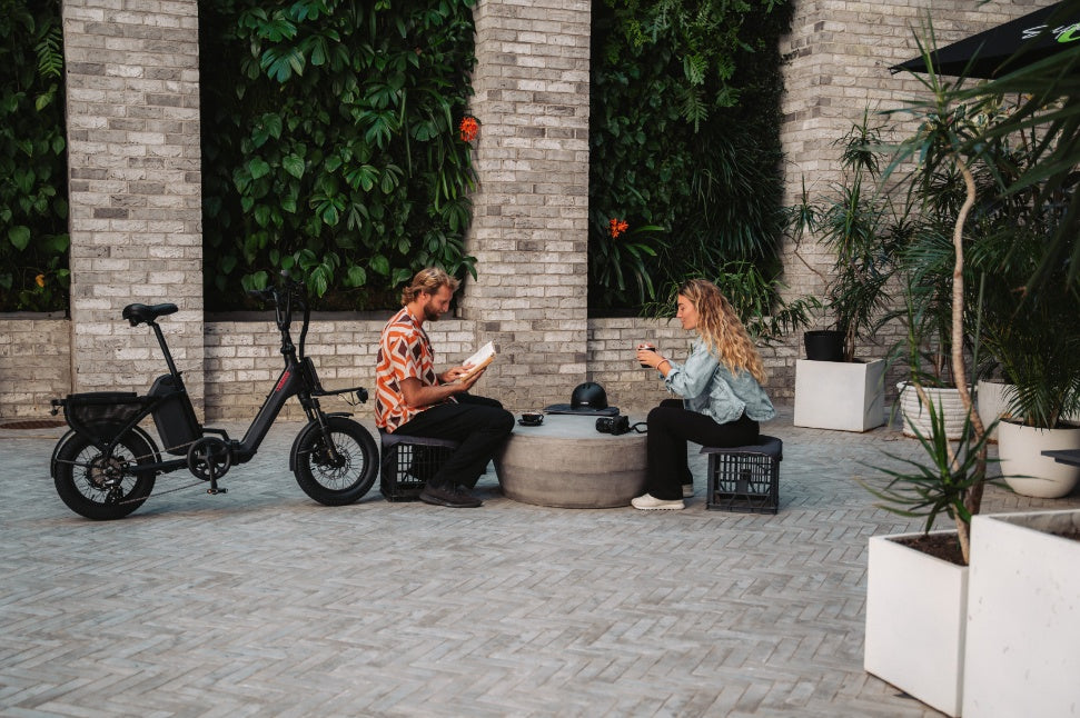 Two people sitting on a patio with an electric bike and a fire pit.