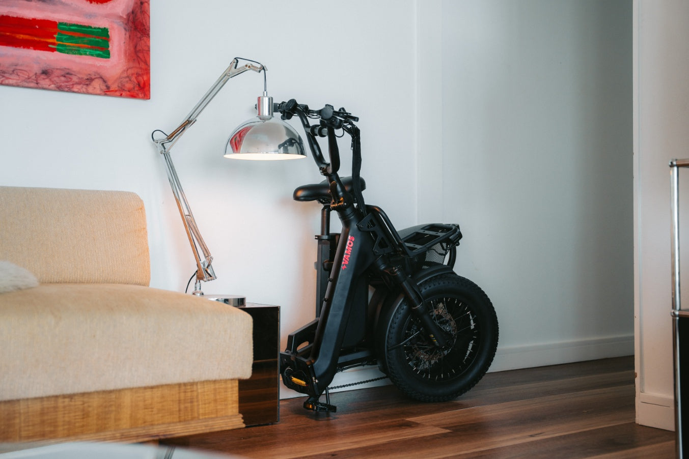 Black electric scooter in a living room setting with a beige couch and lamp.