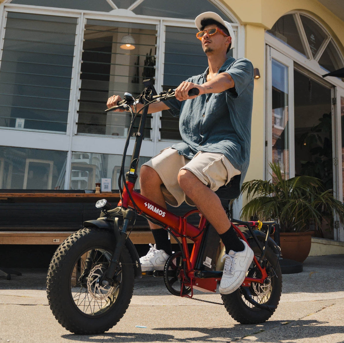 A person riding a red Vamos El Doblez folding electric fat-tire bike.